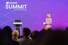 Speaker presenting at Doxis Summit 2026 in Munich with purple backdrop.