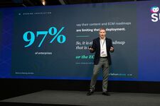 A speaker presenting on stage with a slide showing 97% of enterprises facing limitations in content deployment.