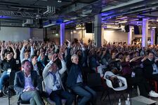 Audience with hands raised at a conference, engaging with the speaker.