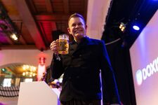 A man in a black jacket holding a large beer mug at an event.
