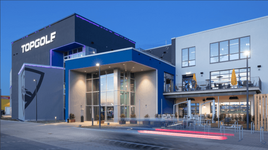 Modernes Topgolf-Außengebäude bei Dämmerung mit beleuchteten Schildern.
